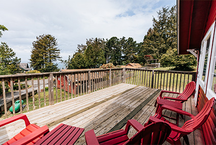 A large deck with several chairs on it overlooks a scenic forest and the ocean.