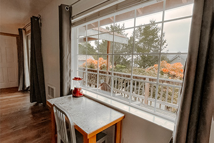 A small table with a single chair rests against a window with a view of a forested area.